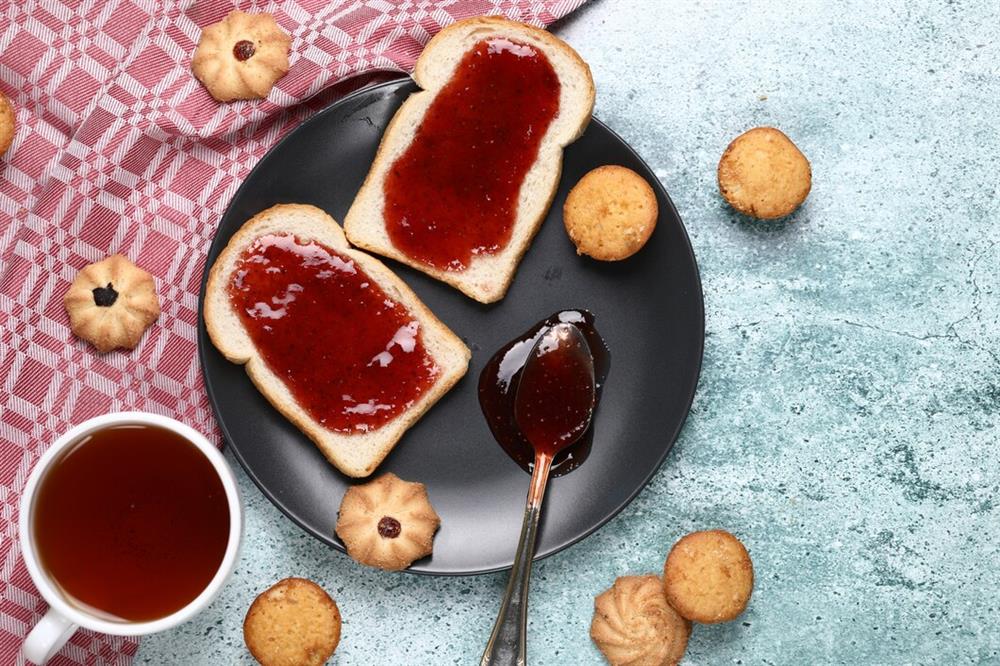 /two-slices-toast-with-red-jam-black-plate-with-cookies-around